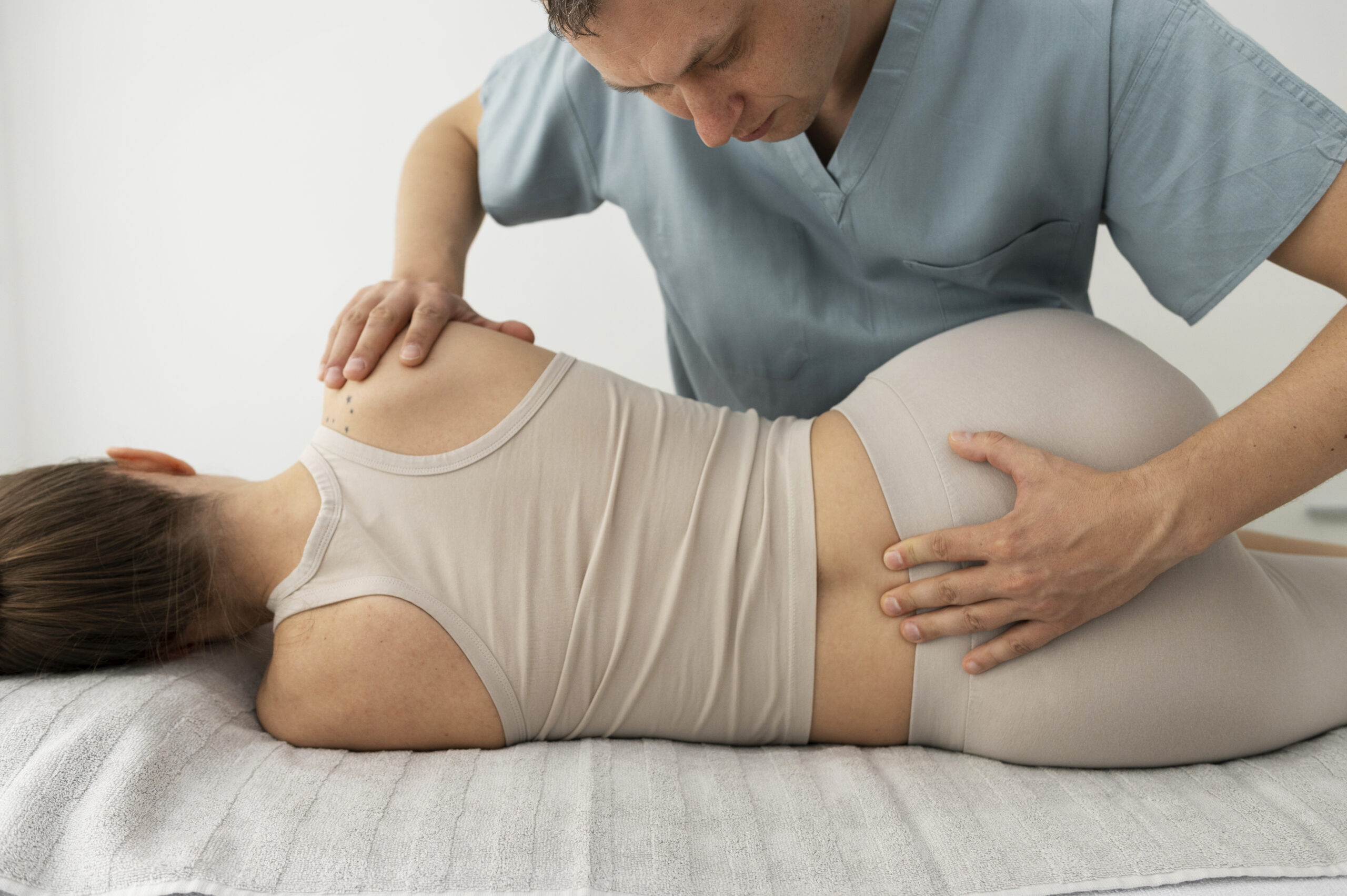Man helping a woman stretch her lower back out while she is laying on her side