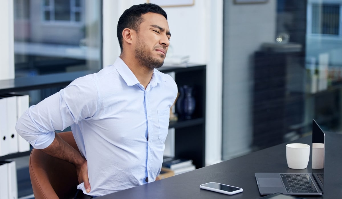 Man sitting at his desk stretching his back due to stiffness and pain