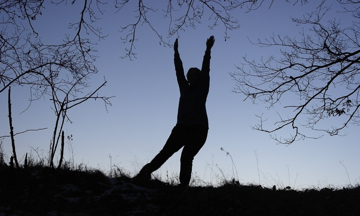 a silhouette of a person doing yoga on a hill