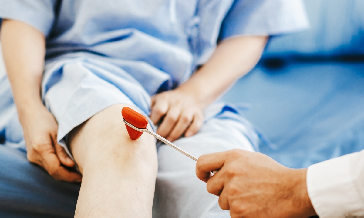 a doctor's hand holding a tiny, triangular mallet to a person's knee