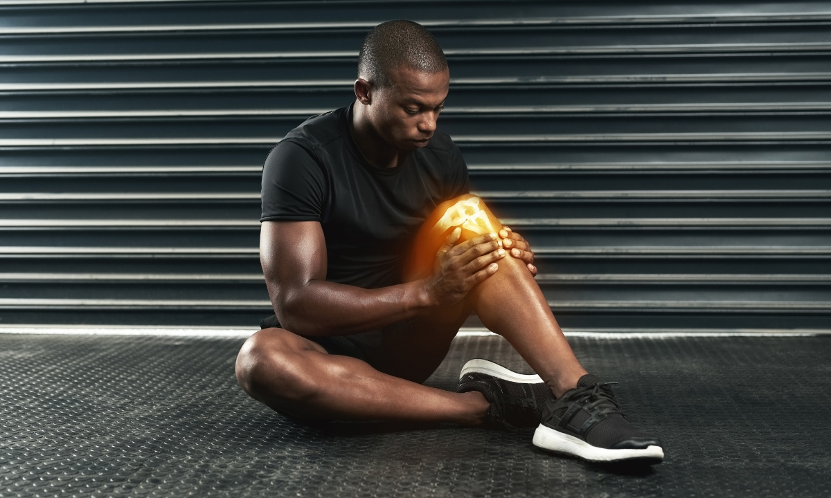 a man sitting on the floor, looking at his knee, which is glowing with an edited-on x-ray