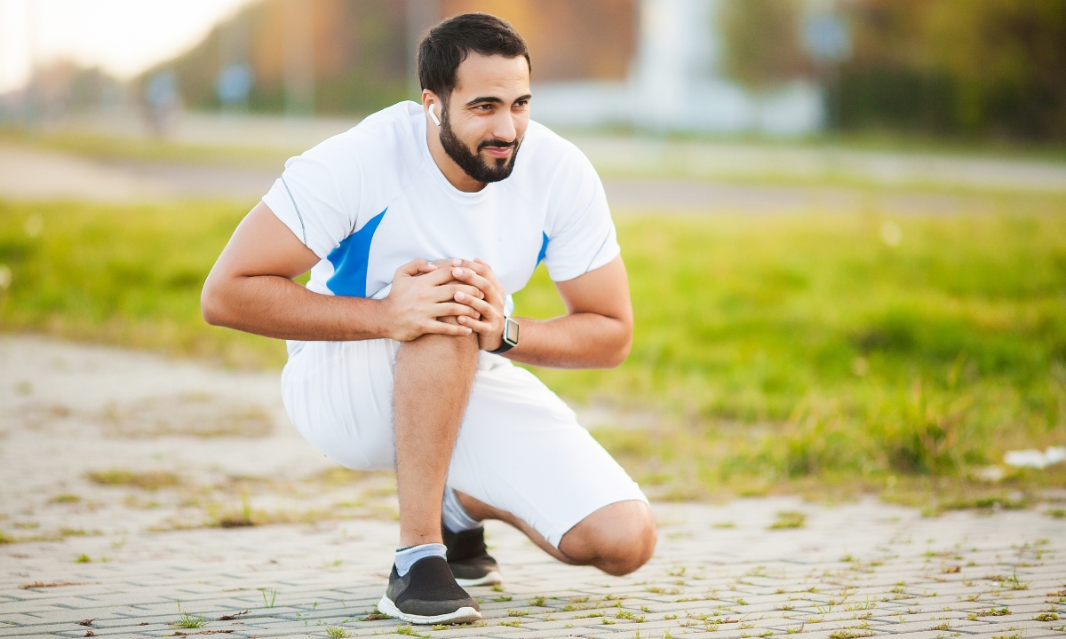 a runner squatting on the path, holding his knee and wincing