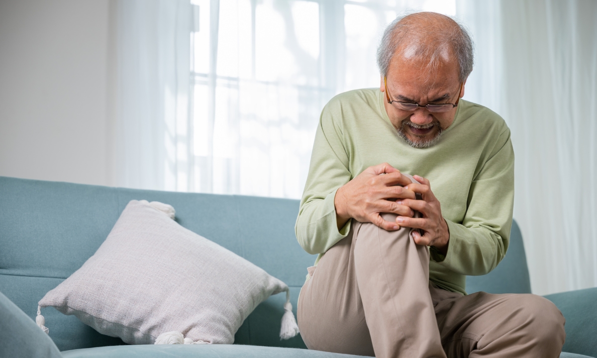 an elderly man on his couch gripping his knee