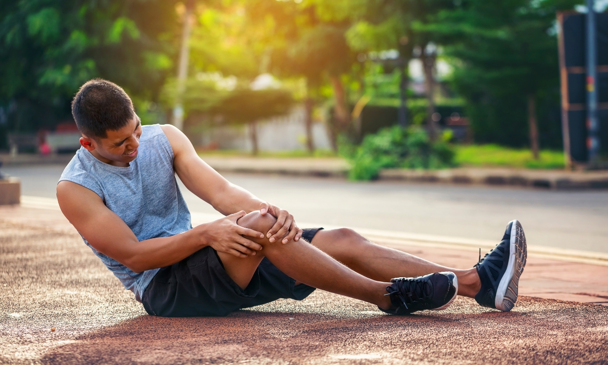 a young man in a park sitting on the ground and clutching his knee