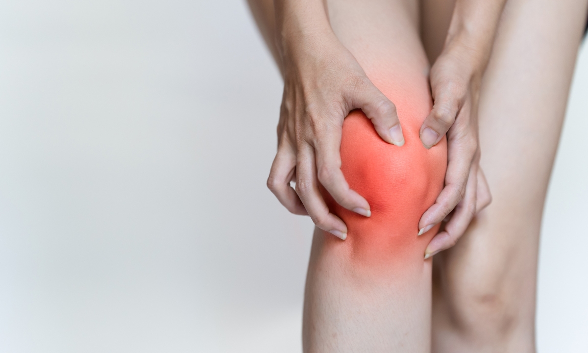 a person's hands on their knee with a red color on the knee to simulate inflammation