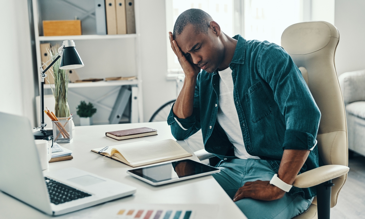 a man at a desk with his head in his hand, grimacing in pain