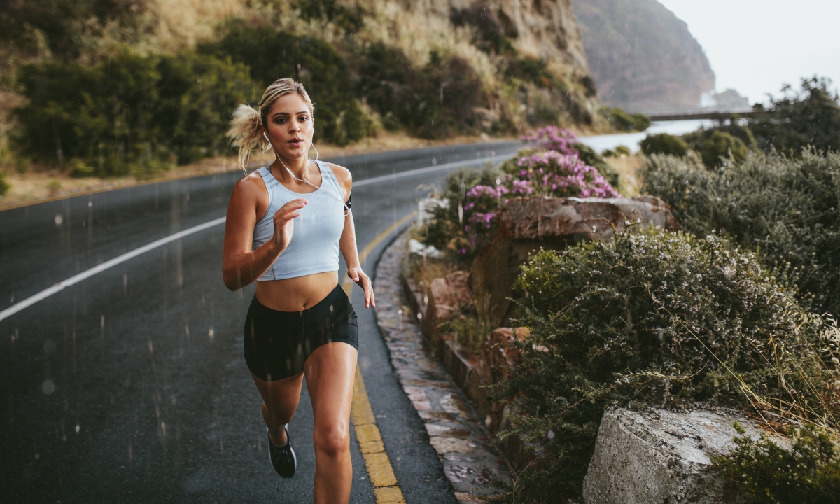 a blonde woman running on a cliffside road in the rain